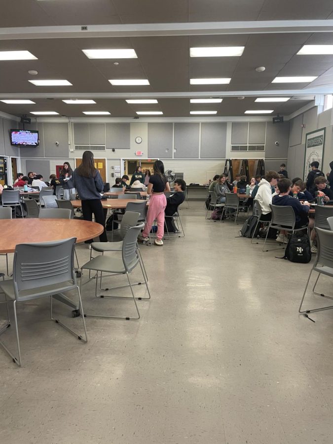 The majority of the lunch tables are filled up, and students come and go to buy food from the cafeteria. 